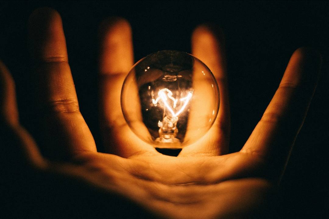 Świecąca żarówka nad ręką w ciemności